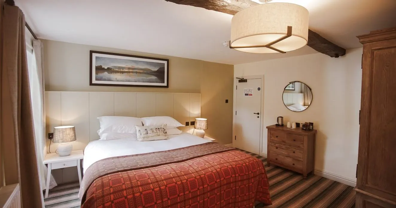 Cosy hotel bedroom with exposed wooden beams, double bed and red patterned bedspread.