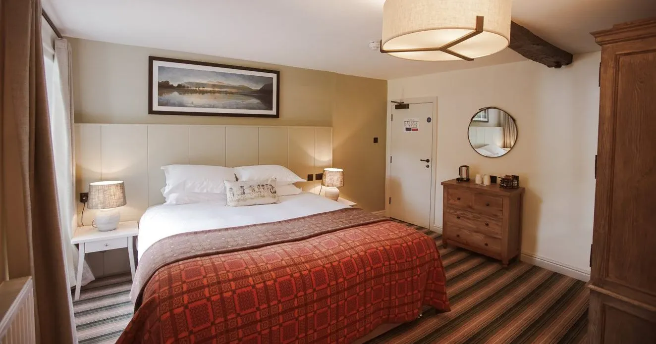 Cosy hotel bedroom with exposed wooden beams, double bed and red patterned bedspread.