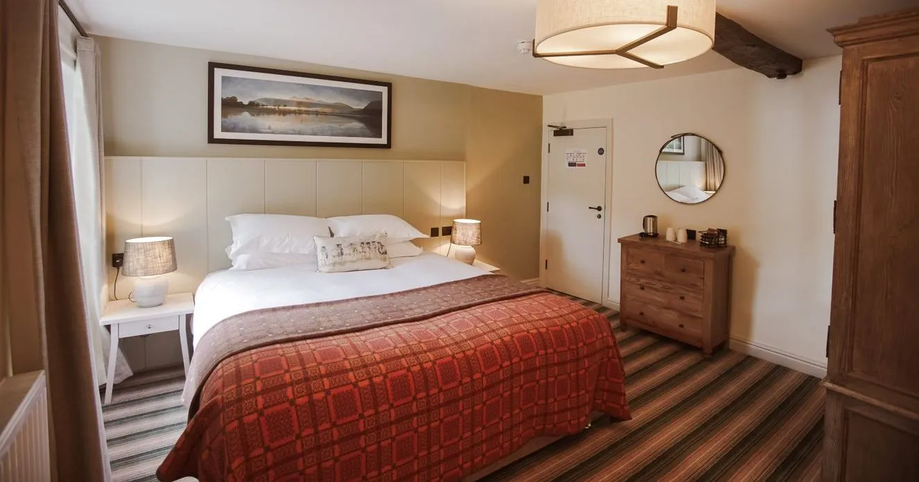 Cosy hotel bedroom with exposed wooden beams, double bed and red patterned bedspread.