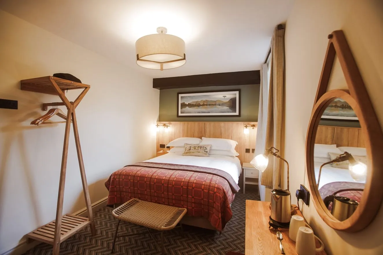 Cosy hotel bedroom with a double bed, red patterned throw, wooden luggage rack and round mirror.