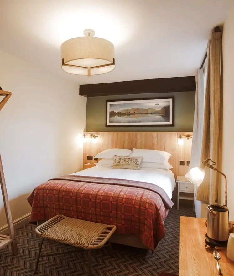 Cosy hotel bedroom with a double bed, red patterned throw, wooden luggage rack and round mirror.