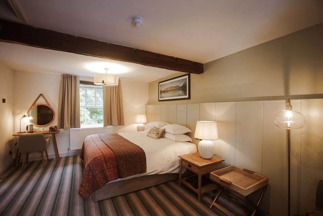 Cosy hotel bedroom with a double bed, bedside lamps, wooden beam and dressing table.
