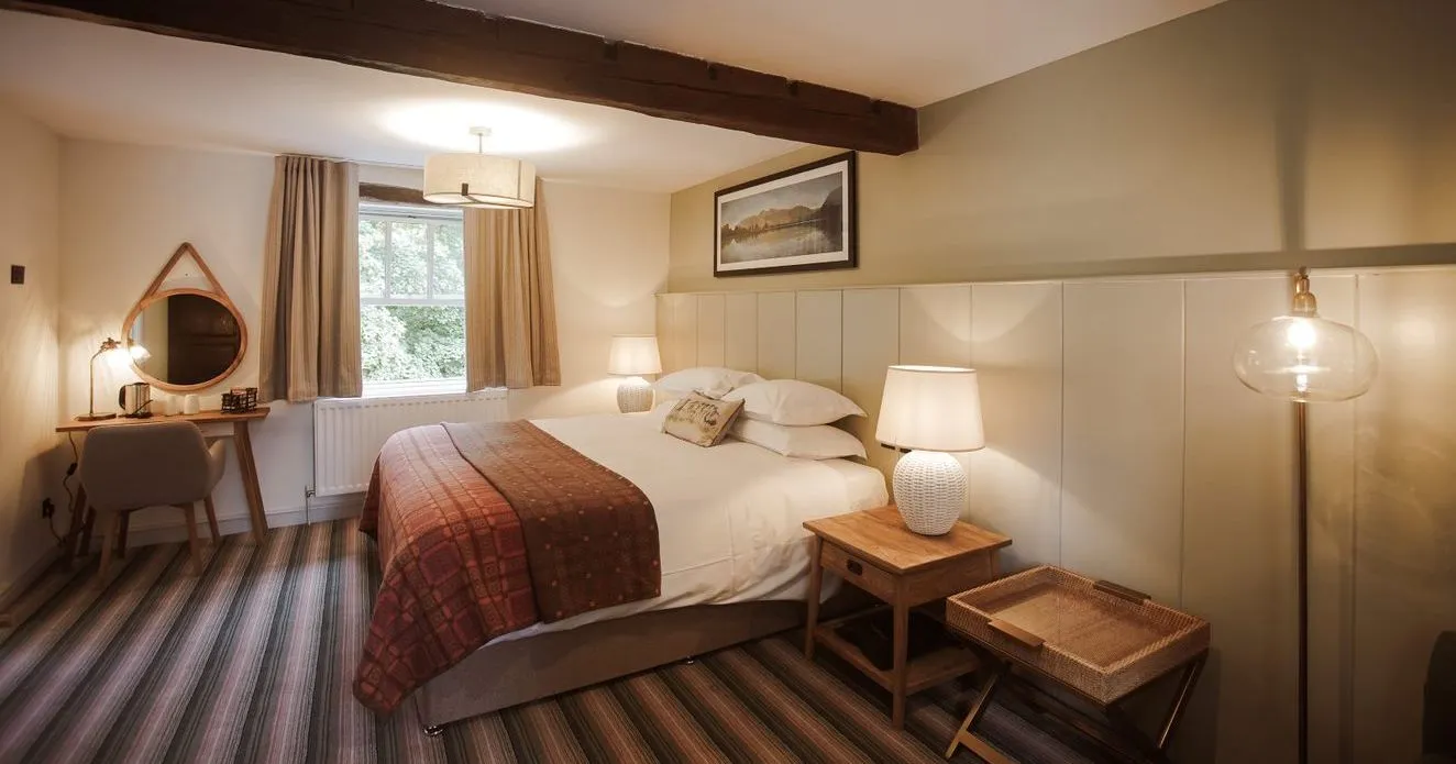 Cosy hotel bedroom with a double bed, bedside lamps, wooden beam and dressing table.