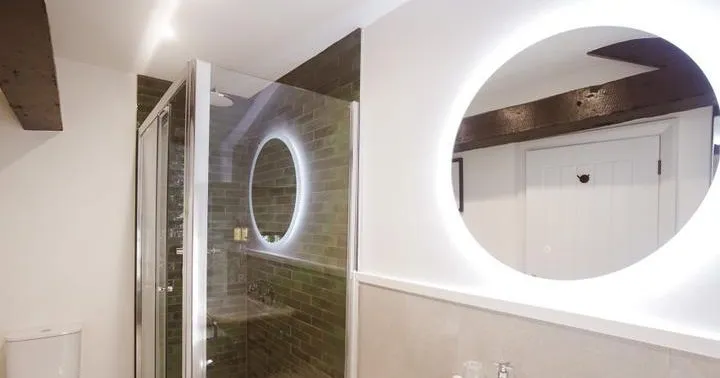 Modern bathroom with glass shower enclosure, illuminated round mirrors, basin and toilet