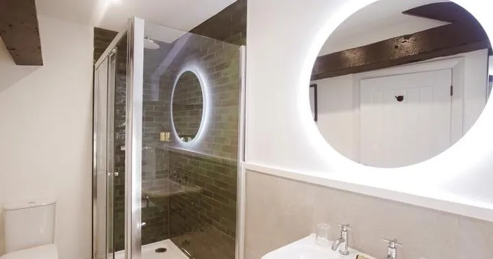 Modern bathroom with glass shower enclosure, illuminated round mirrors, basin and toilet