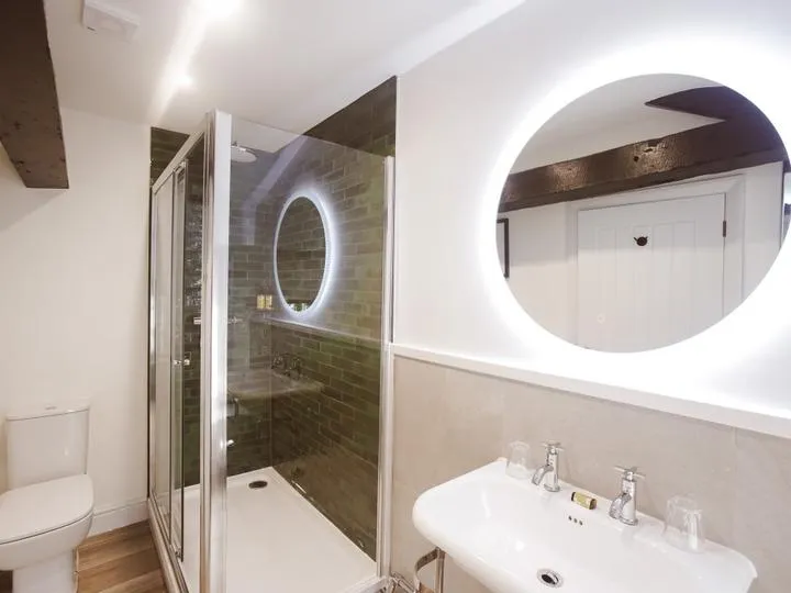 Modern bathroom with glass shower enclosure, illuminated round mirrors, basin and toilet