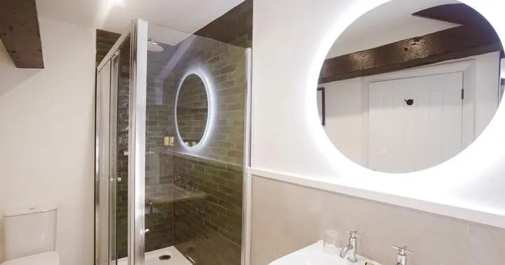 Modern bathroom with glass shower enclosure, illuminated round mirrors, basin and toilet