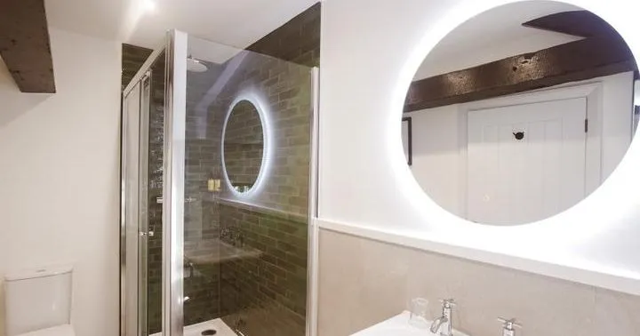 Modern bathroom with glass shower enclosure, illuminated round mirrors, basin and toilet