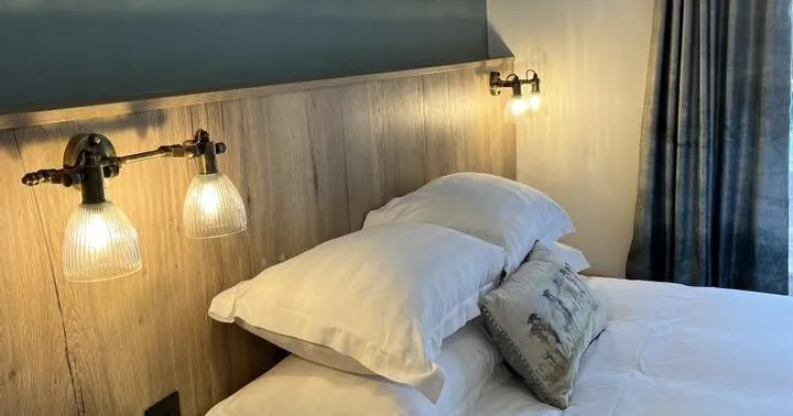 Cosy bedroom with white pillows, wooden headboard and glowing wall-mounted bedside lights.