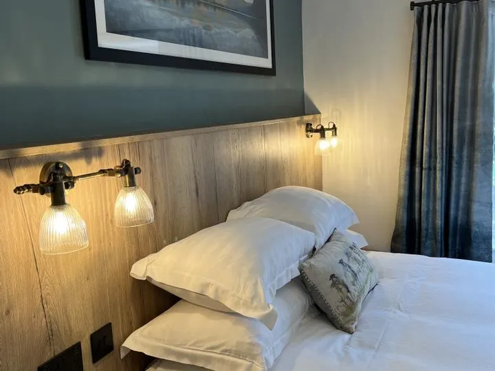 Cosy bedroom with white pillows, wooden headboard and glowing wall-mounted bedside lights.