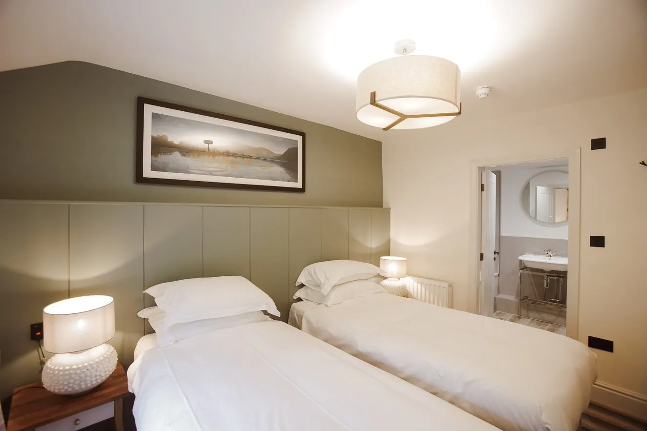 Twin bedroom with white bedding, bedside lamps and an en-suite bathroom