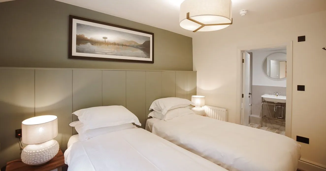 Twin bedroom with white bedding, bedside lamps and an en-suite bathroom