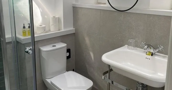 Compact modern bathroom with glass shower, toilet, pedestal sink and round mirror