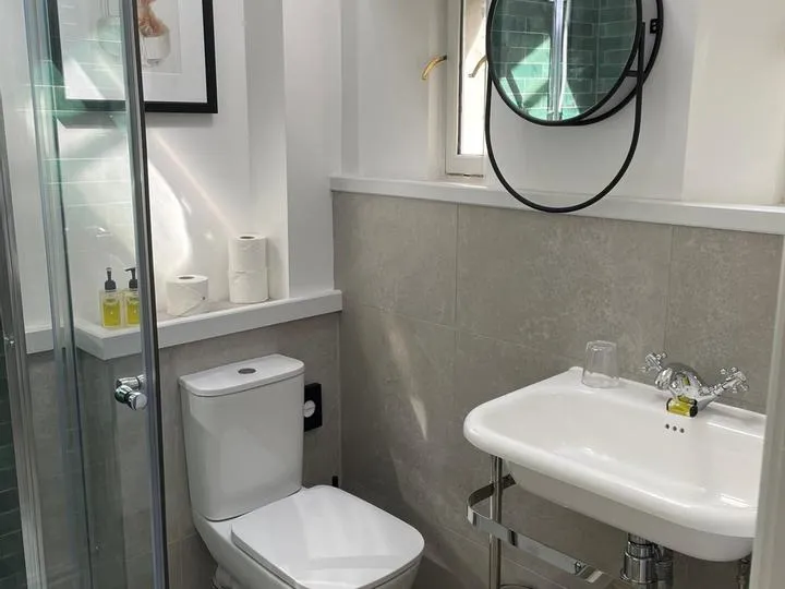 Compact modern bathroom with glass shower, toilet, pedestal sink and round mirror