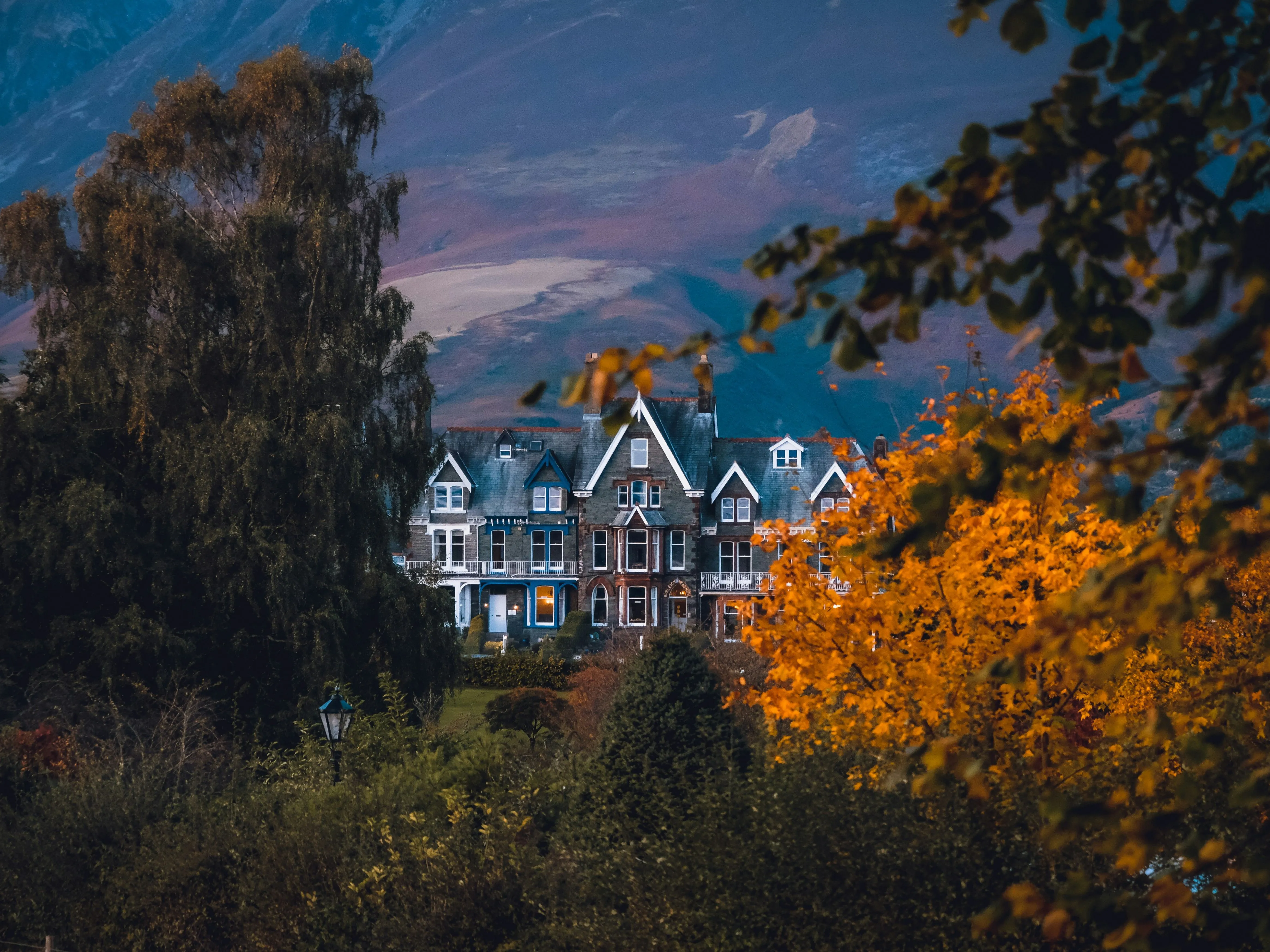 Victorian-style houses framed by autumn trees beneath a dramatic blue evening sky