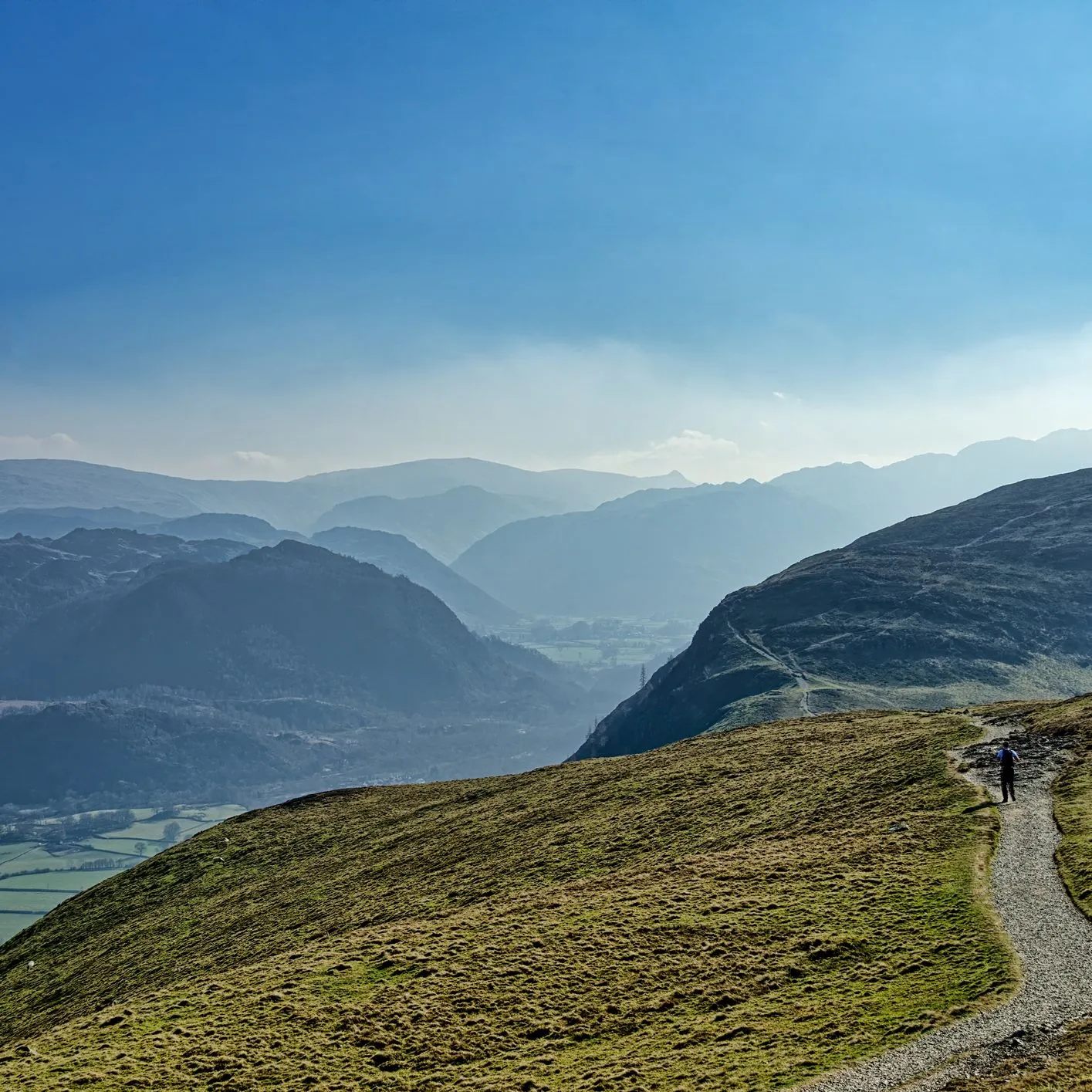 Lone hiker walking along a mountain path above a misty valley under a blue sky