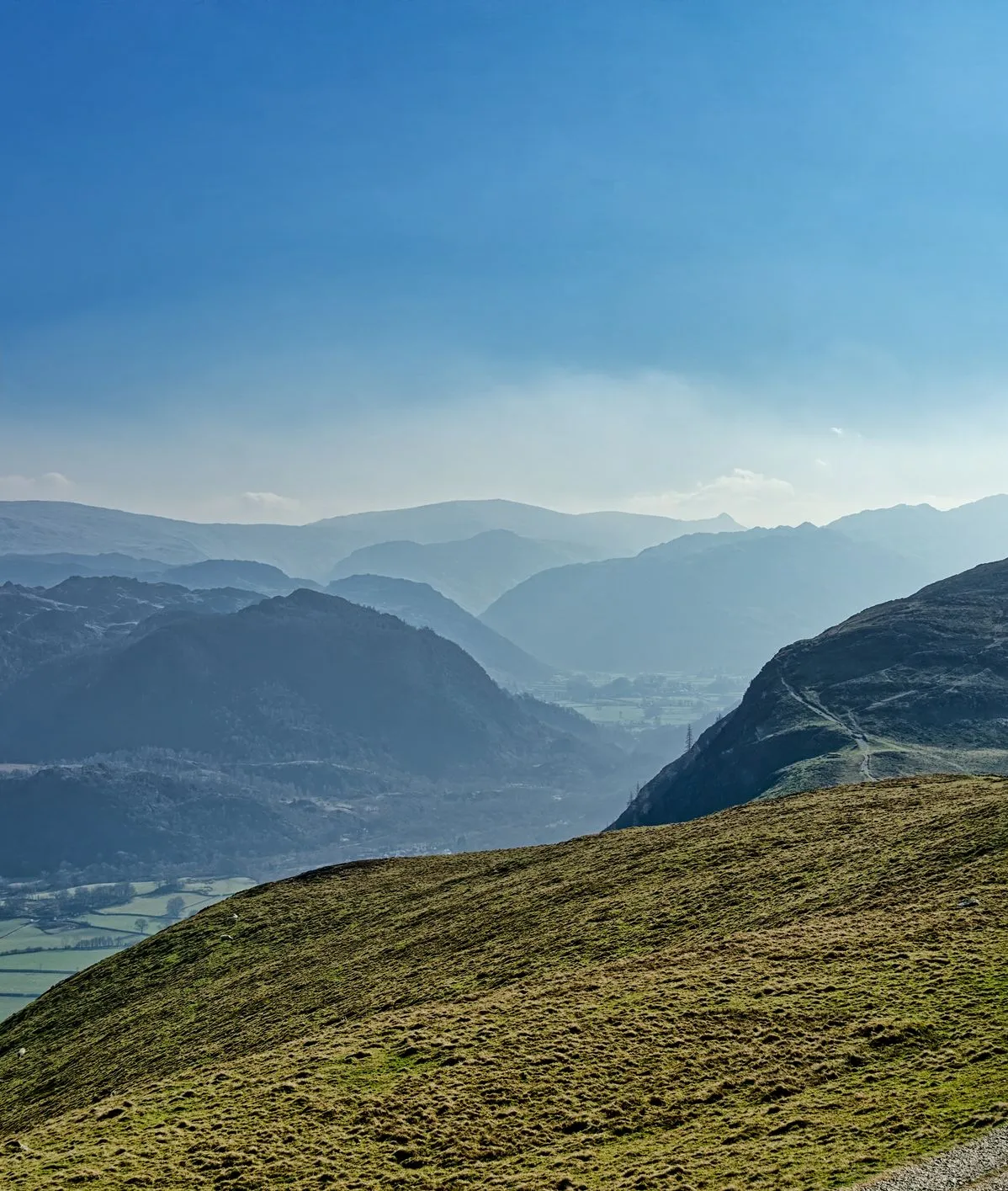Lone hiker walking along a mountain path above a misty valley under a blue sky