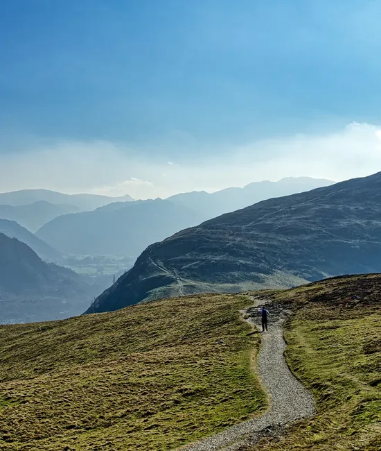 Lone hiker walking along a mountain path above a misty valley under a blue sky