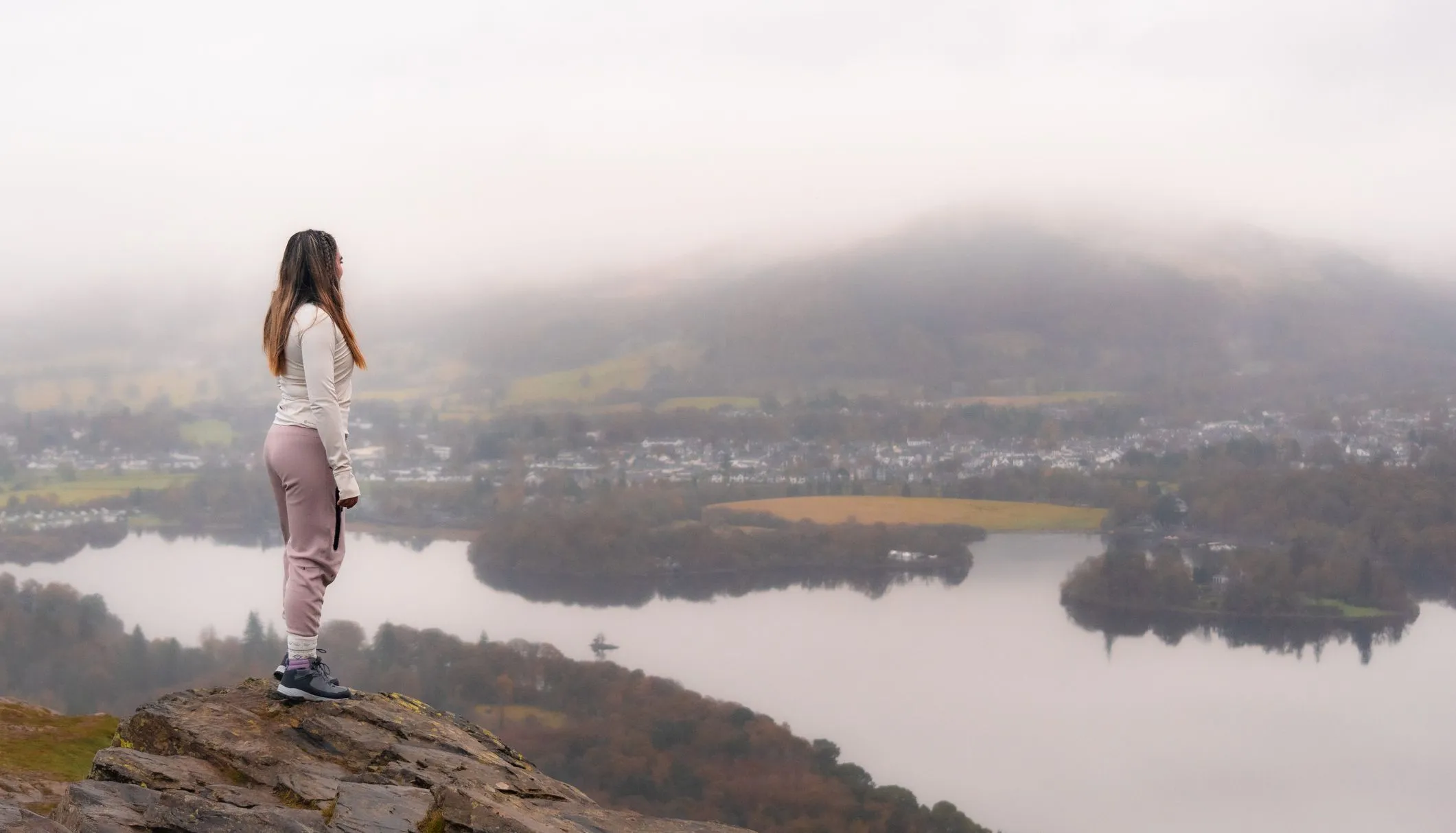 Woman standing on a rocky hilltop overlooking a misty lake and valley.
