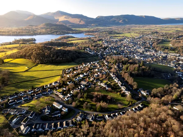 Aerial view of a town beside a lake, surrounded by green fields, woodland and mountains in warm afternoon light.