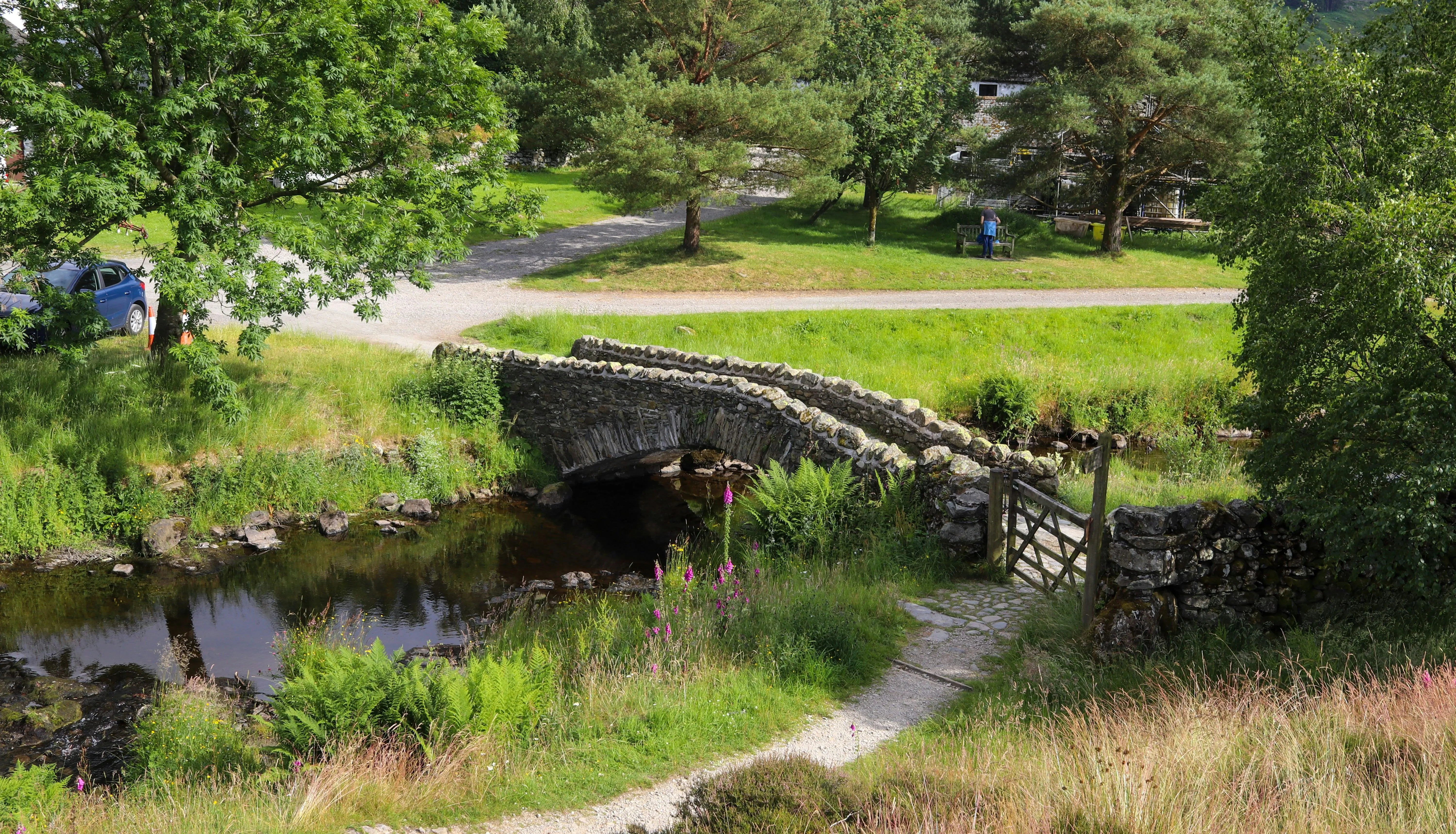 Old stone arch bridge crossing a shallow stream in a lush green rural landscape