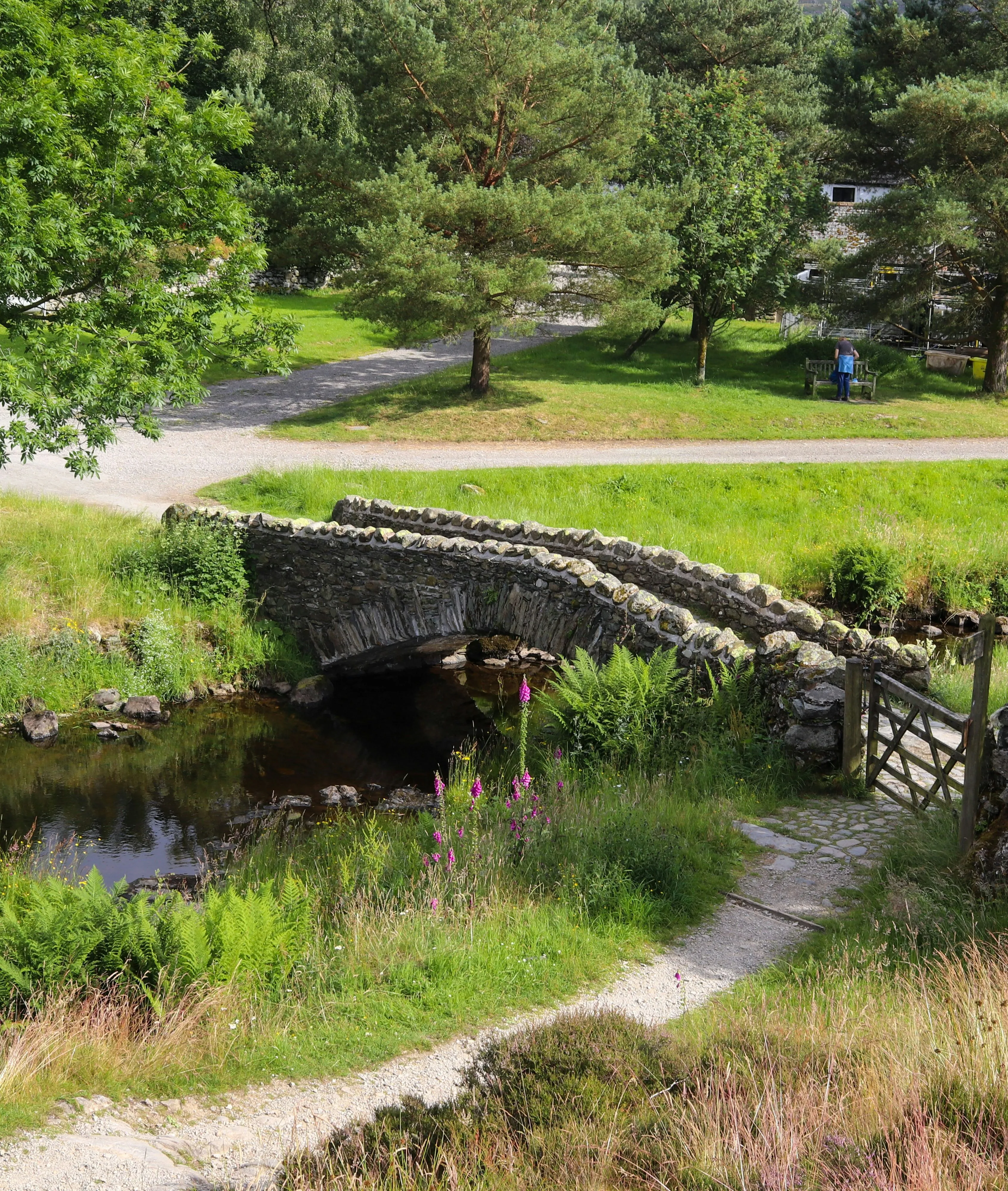 Old stone arch bridge crossing a shallow stream in a lush green rural landscape