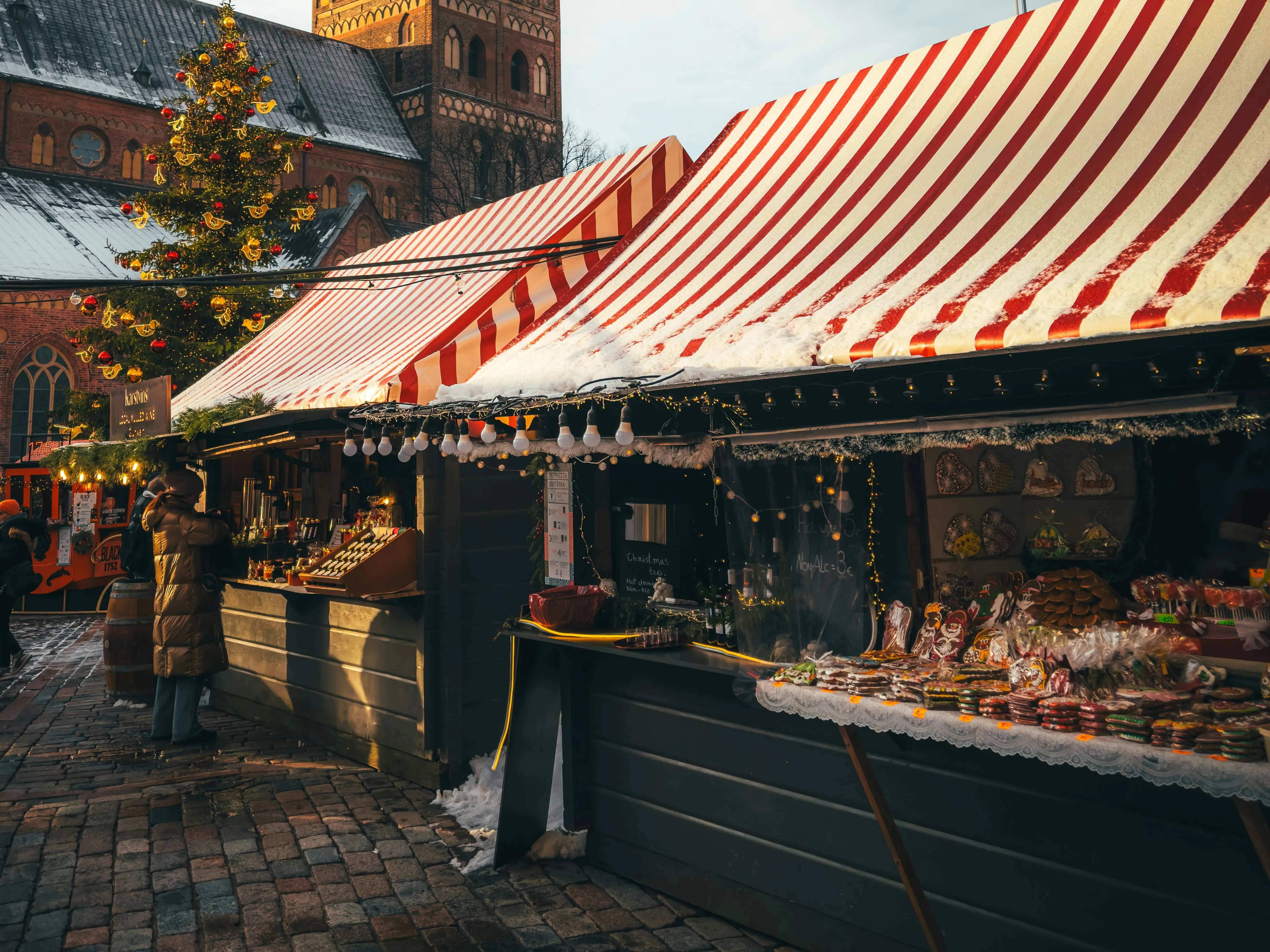 Snow-covered Christmas market stalls beneath a historic church clock tower