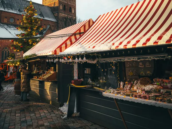 Snow-covered Christmas market stalls beneath a historic church clock tower