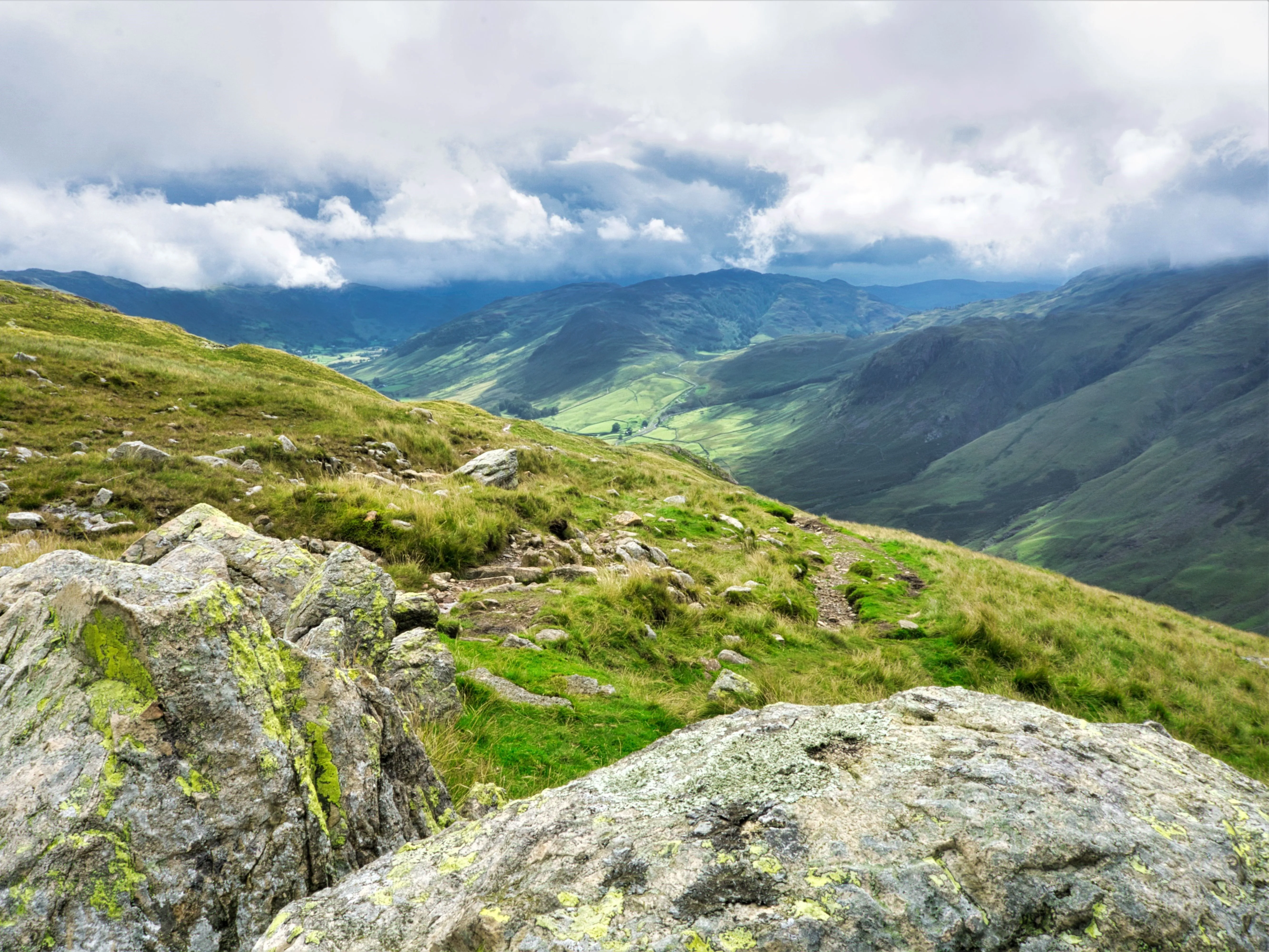 Rocky mountain path overlooking a green valley beneath dramatic clouds