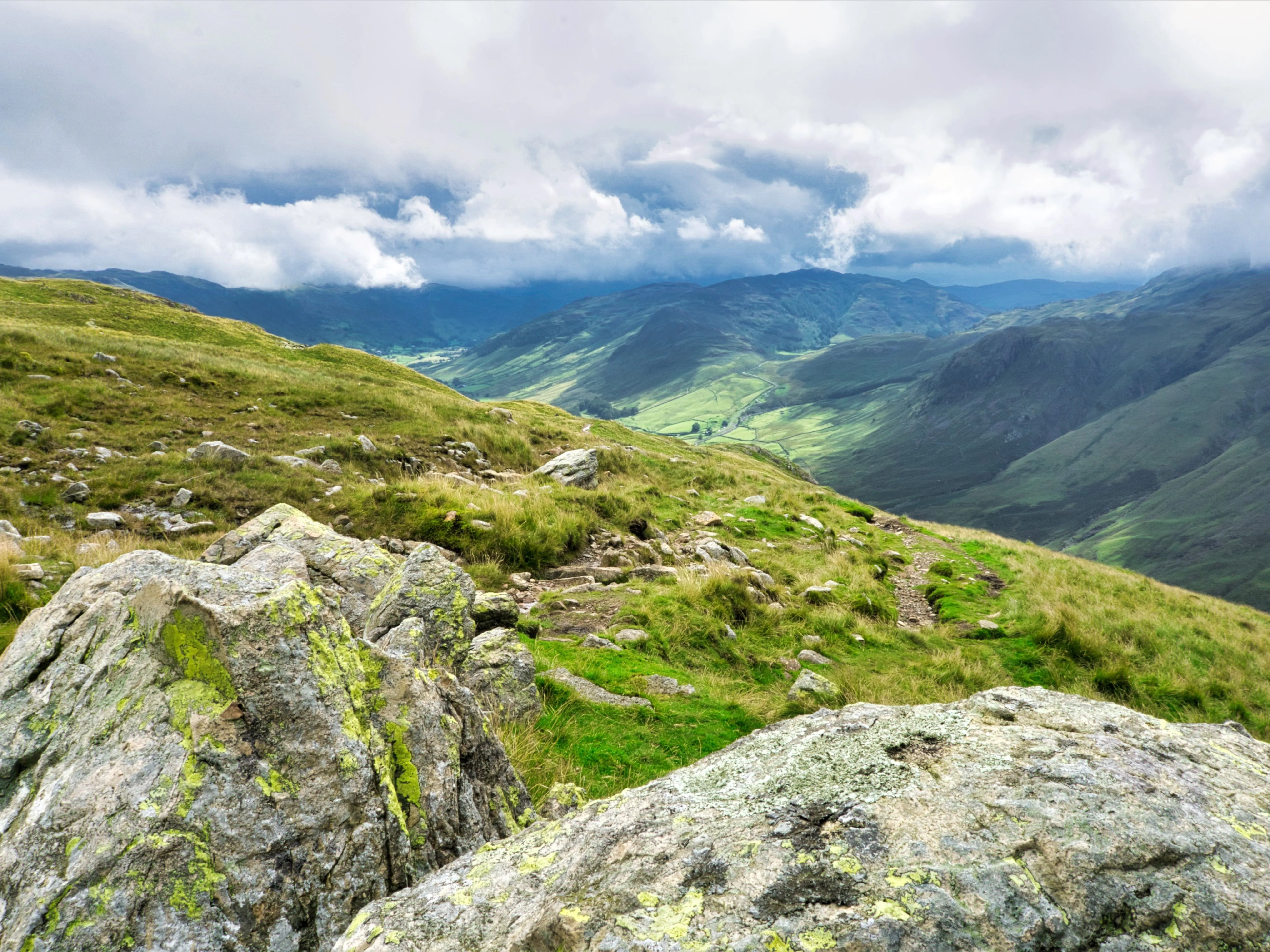 Rocky mountain path overlooking a green valley beneath dramatic clouds