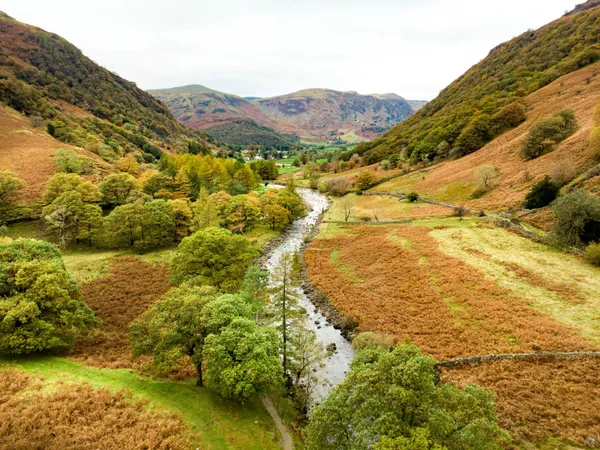 Autumn valley with a winding river, wooded hills and rugged mountains under an overcast sky.