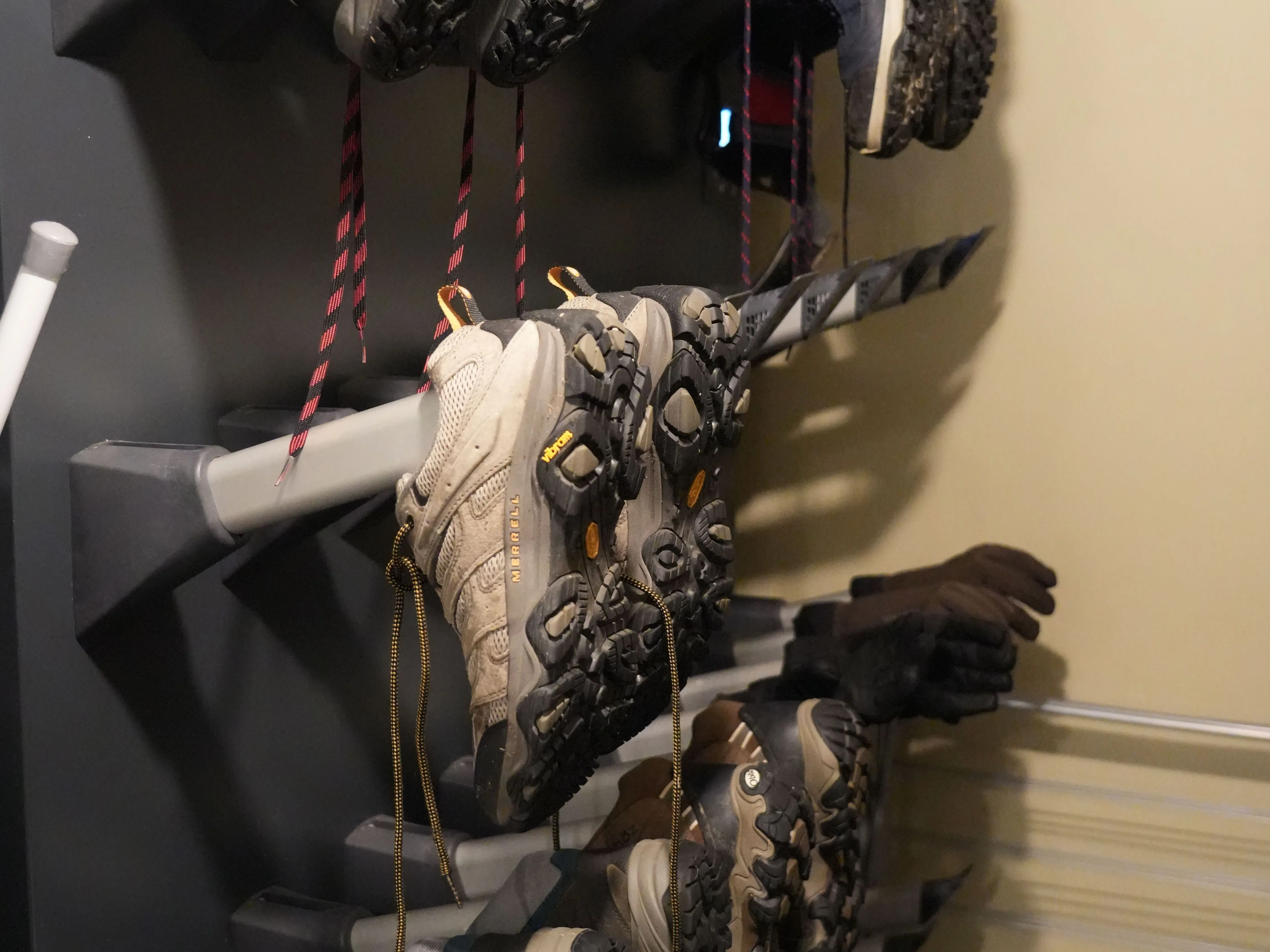 Several pairs of hiking boots and trail shoes stored upside down on a wall-mounted shoe rack.