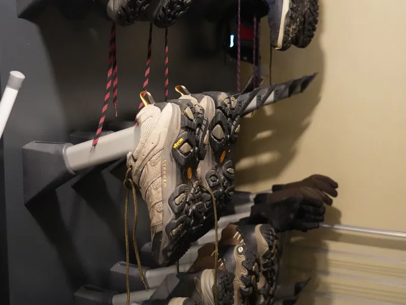 Several pairs of hiking boots and trail shoes stored upside down on a wall-mounted shoe rack.