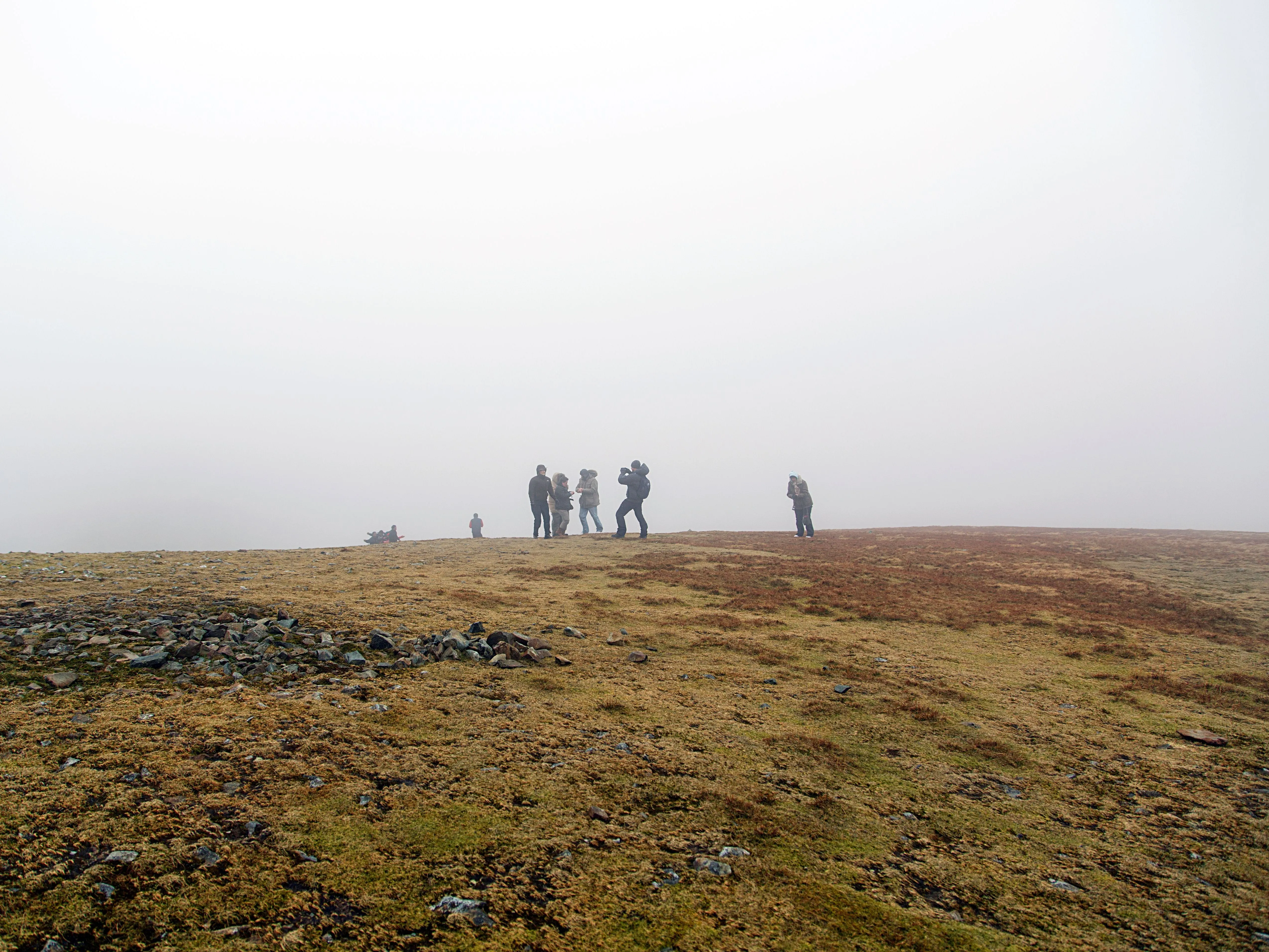 Hikers standing on a misty grassy hillside with rocky ground beneath an overcast sky.