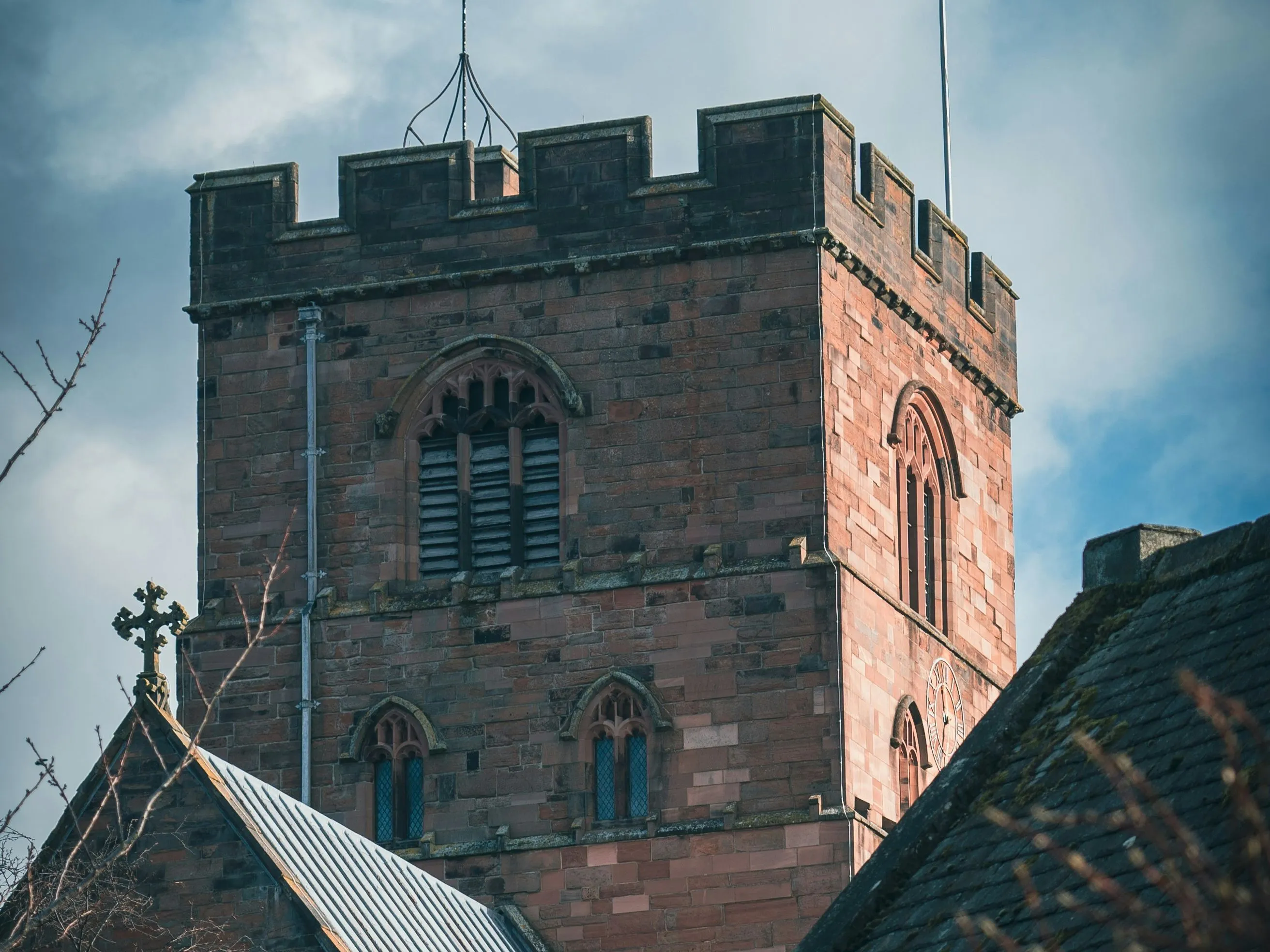 Red sandstone church tower with crenellations and Gothic windows beneath a cloudy blue sky