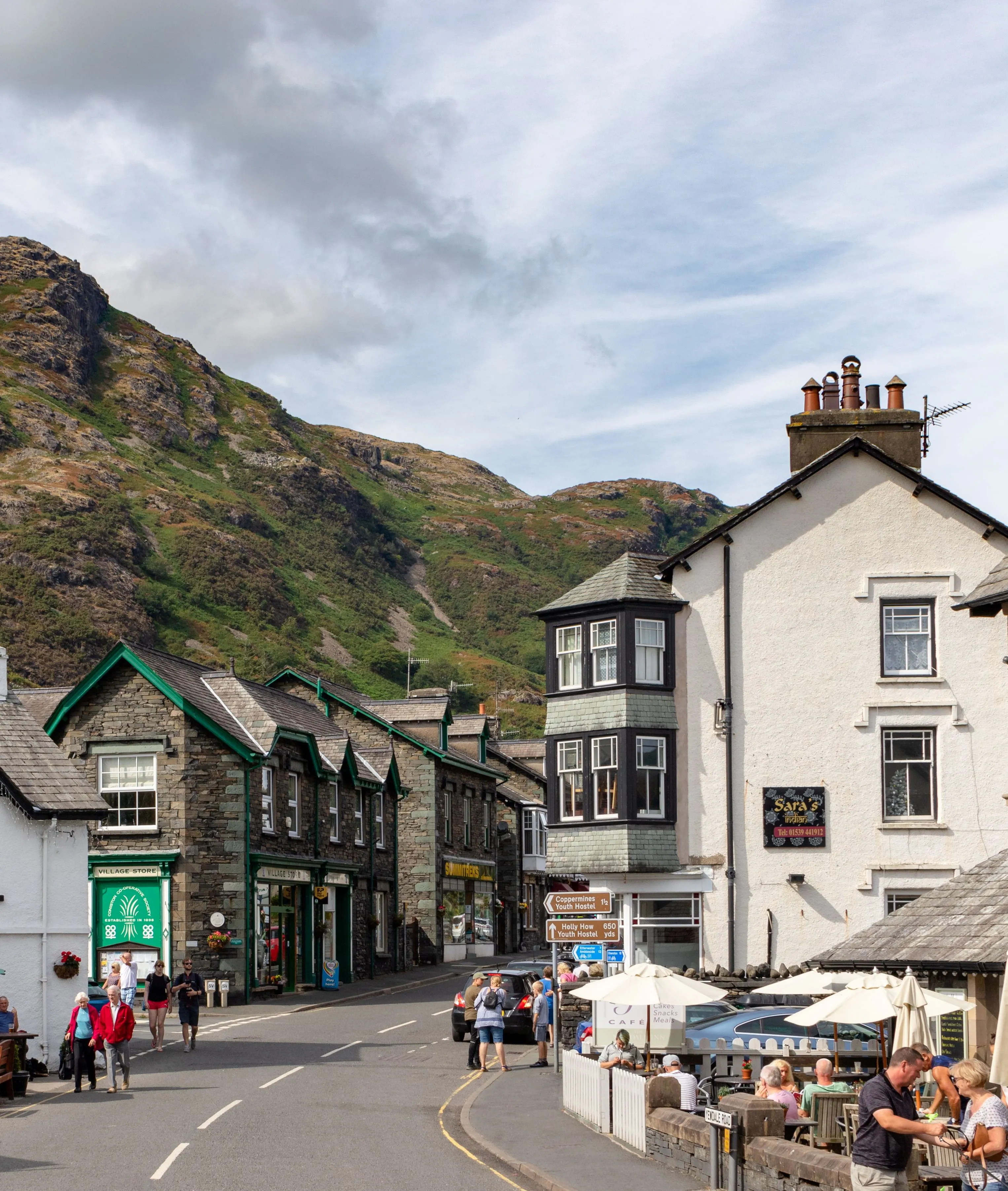 Village street in Coniston with cafés, traditional buildings and a rugged Lake District fell behind.
