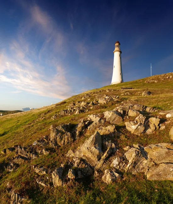 White lighthouse standing on a rocky grassy hill beneath a dramatic blue evening sky near Ulverston.