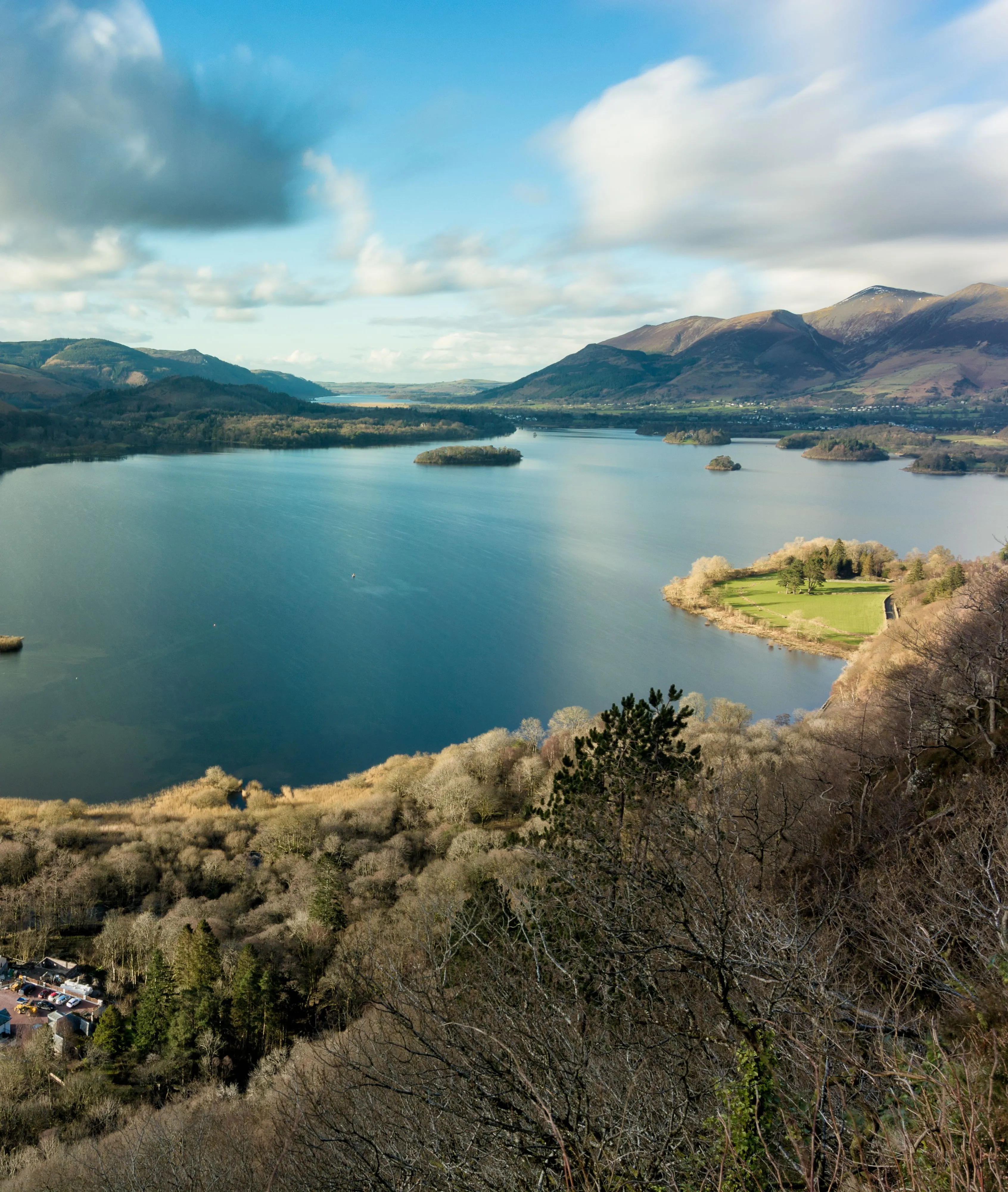 Panoramic view across Derwentwater from Surprise View, with wooded islands, surrounding fells and dramatic clouds in the Lake District.
