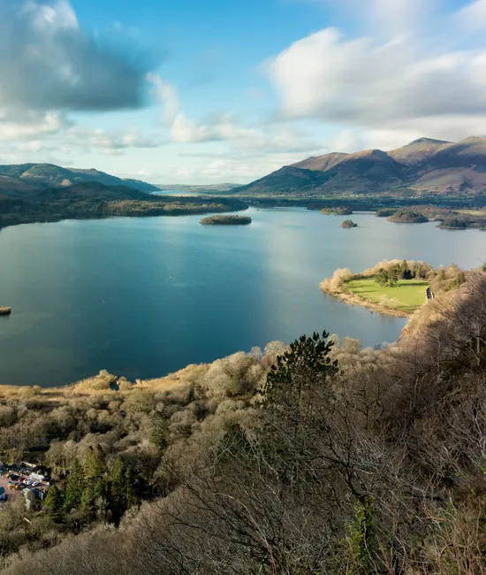Panoramic view across Derwentwater from Surprise View, with wooded islands, surrounding fells and dramatic clouds in the Lake District.