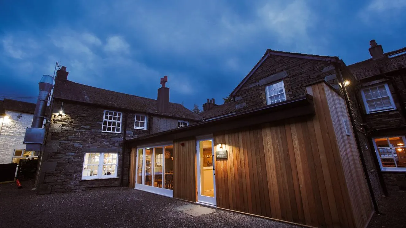 Stone cottages and a timber-clad entrance glowing warmly beneath a cloudy blue evening sky.