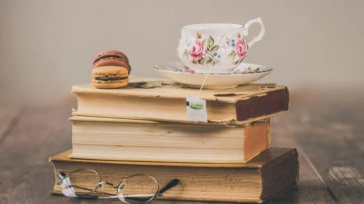 Floral teacup and macarons resting on a stack of vintage books with round spectacles