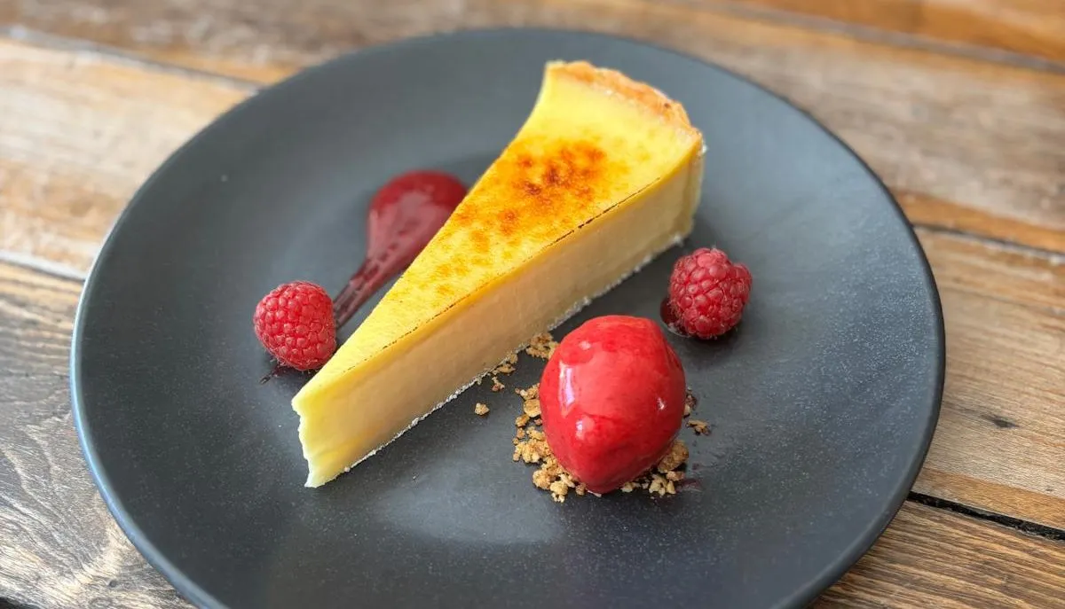 Slice of baked cheesecake with raspberry sorbet and fresh raspberries on a black plate