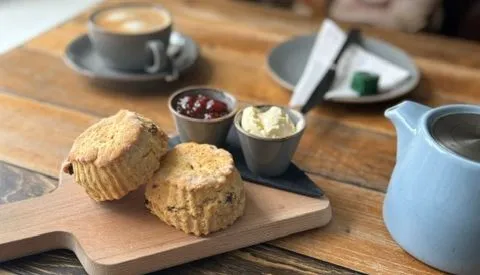Freshly baked fruit scones on a wooden board with jam, clotted cream and tea.