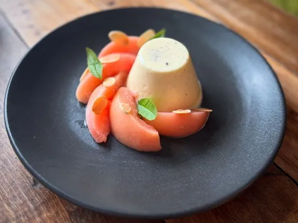 Creamy panna cotta with poached rhubarb, almond flakes and green herb leaves on a dark plate
