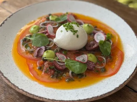 Burrata topped with chives on a tomato salad with olives, radishes and herbs