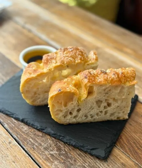 Two pieces of golden crusty bread served on a black slate board with olive oil dip