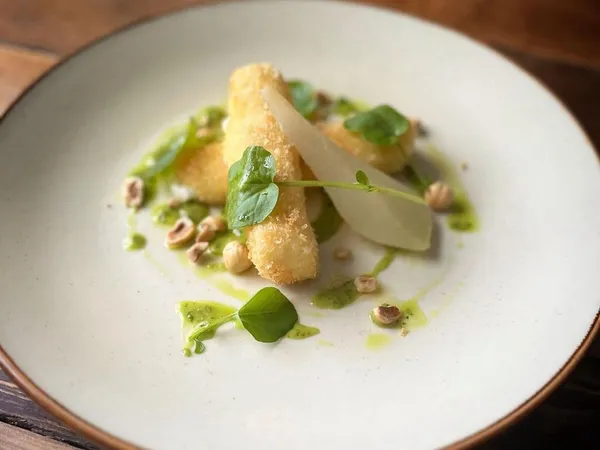Crispy fried croquettes served with pear slices, hazelnuts, green herb sauce and fresh leaves on a ceramic plate