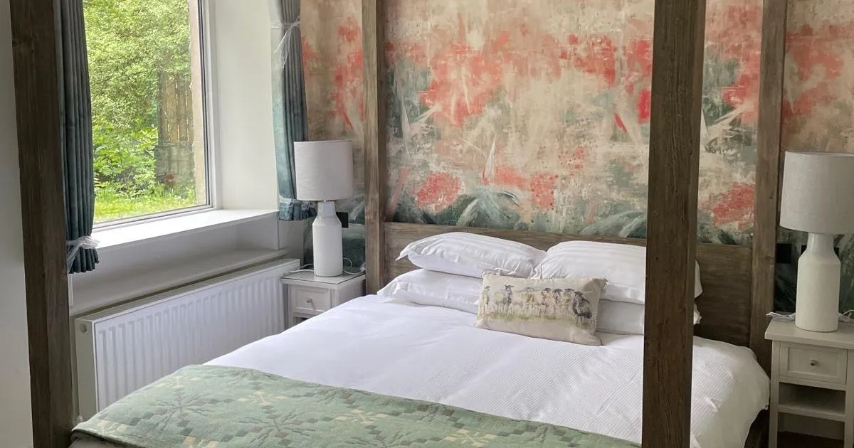 Cosy bedroom with a dark wooden four-poster bed, white bedding and patterned green throw.