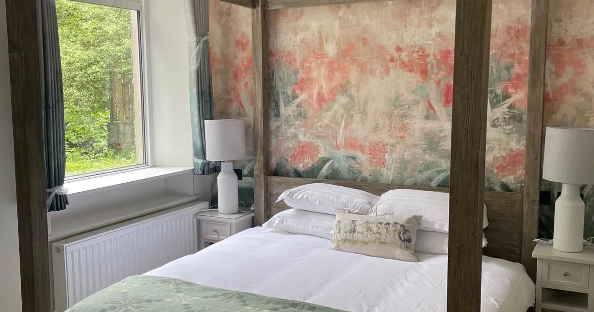 Cosy bedroom with a dark wooden four-poster bed, white bedding and patterned green throw.