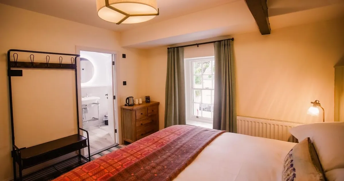 Warmly lit bedroom with a double bed, wooden dresser, exposed beam and en-suite bathroom
